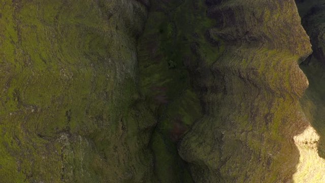 Aerial observing the ravine sandwiched between rocky walls of amazing volcanic formations of Hawaiian island. Sheer slopes and the bottom are covered with grass and are in the shade. Top down.4K