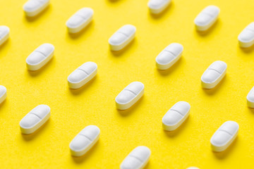White pills or capsules lies in rows diagonal on yellow background