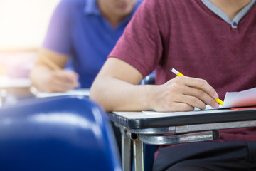 Obraz premium high school,university student study.hands holding pencil writing paper answer sheet.sitting lecture chair taking final exam attending in examination classroom.concept scholarship for education abroad