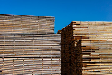 Long planks of pinewood are seen stored outdoors. Many sawn and treated boards in the yard of a sawmill. Stockpiled ready for distribution.