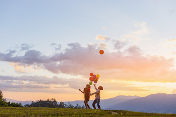 Two cute little girls playing on mountain park with air balloons at sunset. Best friends.