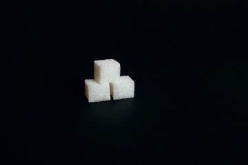 Three sugar cubes on a black background, a sweet additive to taste or a harmful and dangerous ingredient, diabetes, place for text