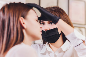 beautician- makeup artist applies paint henna on previously plucked, design, trimmed eyebrows in a...