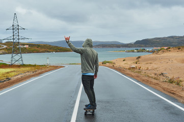 Young man riding a longboard on empty winding mountain road in summer, rear view.
