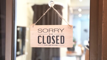 Through glass view of Asian male business owner hanging up sign with inscription closed at end of working day