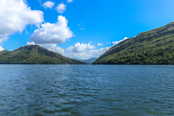 Beautiful landscape of blue water lake between two green mountains with a partly cloudy blue sky.