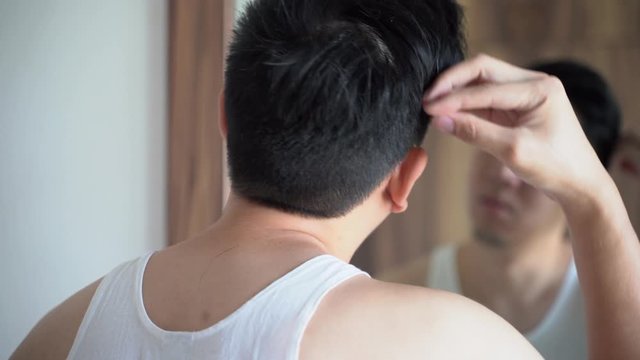 Back view of Asian grooming man in white shirt combing hair in front of mirror
