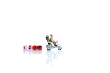 Fototapeta premium Miniature / toys photography for valentines day - young couple riding scooter with love beads word block on shiny white background