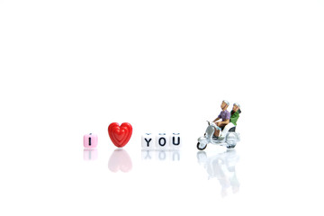 Miniature / toys photography for valentines day - young couple riding scooter with I love you beads on shiny white background