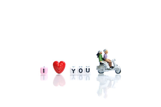 Miniature / toys photography for valentines day - young couple riding scooter with I love you beads on shiny white background