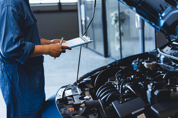 Car mechanic holding clipboard and checking to maintenance vehicle by customer claim order in auto...