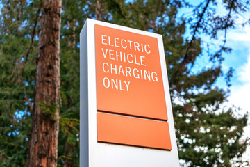 Electric vehicle charging only warning sign with blurred green trees in background. Designated parking space for EV vehicles near electrical vehicle charging station