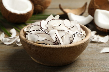 Tasty coconut chips in bowl on wooden table