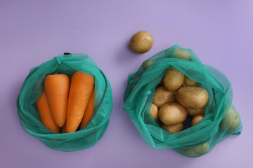 Net bags with vegetables on lilac background, top view
