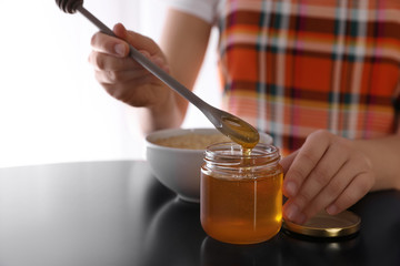 Woman with honey and spoon at black table, closeup