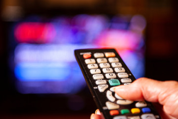 Hand mit Fernbedienung vor großem Bildschirm Netflix auswählen 