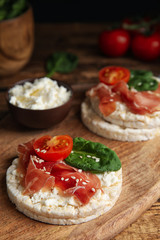 Puffed rice cakes with prosciutto, tomato and basil on wooden board