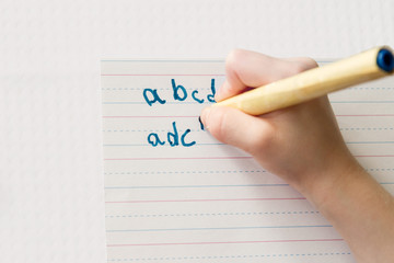 Child writes the alphabet with pencil but mixes up b and d; child practices letter formation but reverses b and d - obrazy, fototapety, plakaty