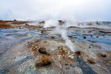 Hot sulfuric steam vent spewing sulphur steam in the hot sulfuric and geothermal area of Namaskard in Myvatn/Iceland. Color and mineral rich textured muddy ground infront.