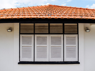 Close up of the antique wooden window shutters and red tiled roof of a whitewashed aged old British colonial bungalow in Singapore