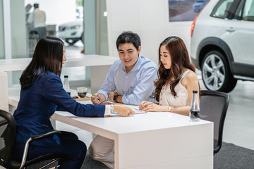 Asian Saleswoman explaining sales contract to couple customer before decision buy the new car in...