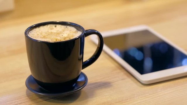Digital tablet and cup of coffee on wooden desk. Simple workspace or coffee break in morning.