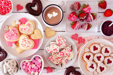 Valentines Day table scene with a selection of sweets and cookies. Top view over a white wood background. Love and hearts theme.