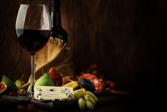 Red wine glass and appetizers, cheese, salami, figs, grapes, vintage wooden table background, selective focus, copy space