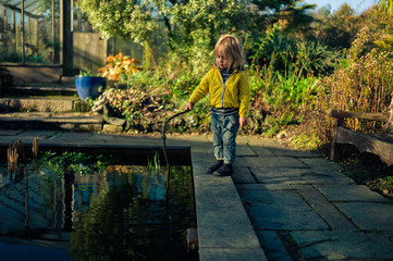 Little toddler with a stick playing by a pond