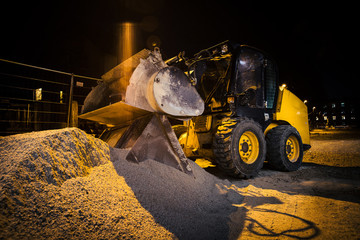 Construction site on a city street. A small yellow digger excavator or bobcat parked during the night on a construction site. Houses in the background. Night exposure