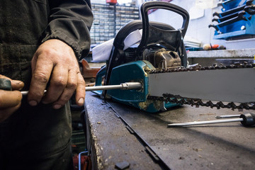Man is unscrewing the blade of a chainsaw on a work bench in a mechanic shop. Service of a chain...