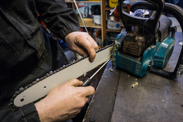 Man is cleaning the blade of a chainsaw from sawdust on a work bench in a mechanic shop. Service of a chain saw, cleaning the blade with a flat headed screwdriver.