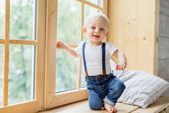 Little boy in wooden scandinavian interior on a window. Infant boy weared in casual denim. Small baby feet. Kid of one year old crawls on the floor. Small legs. First birthday