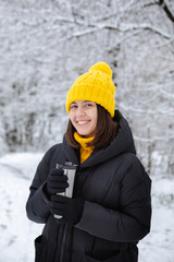 smiling woman in winter outfit drinking warm up drink from refillable mug