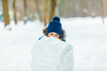 Fototapeta na wymiar little cute boy making snowman. rolling big snowball