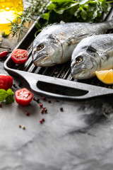 Two raw dorado fish with spices, lemon and parsley in a black grill pan on a white concrete background. Copy space.