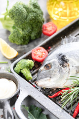 One raw dorado fish with spices, lemon and parsley in a black grill pan on a white concrete background. Healthy eating and tasty culinary concept. macro