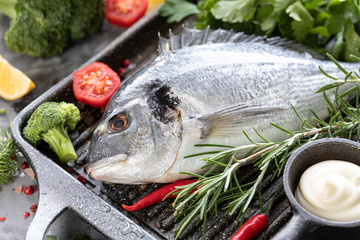 One raw dorado fish with spices, lemon and parsley in a black grill pan on a white concrete background. Healthy eating and tasty culinary concept. macro