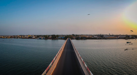Aerial view of the road bridge over casamance river in Ziguinchor, Senegal, Africa during a sunset. Looking towards the city above the driving platform with yellow taxi crossing the bridge.