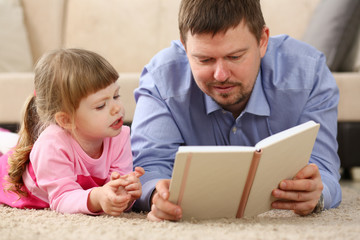Father and daughter lie on floor reading interesting book