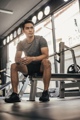 Fototapeta na wymiar Young fitness man sitting in gym. asian sport man sitting and looking to outside in sportclub. 