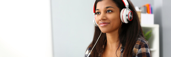 Black smiling woman sitting at workplace wearing headphones