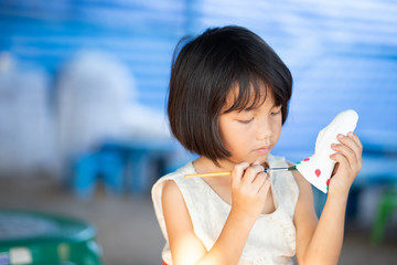 Little Asian girl painting plaster doll