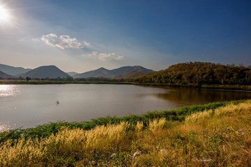 The blurred panoramic nature background of sunlight hitting the lake's surface, grass and wind blowing all the time along the large mountains, ecological beauty and fresh air.
