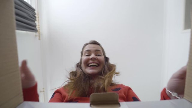 Cheerful woman unboxing a gift and being surprised and happy. Bottom angle view. Camera inside the box.