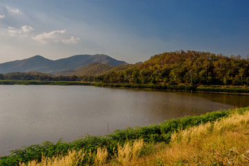 Obraz premium The blurred panoramic nature background of sunlight hitting the lake's surface, grass and wind blowing all the time along the large mountains, ecological beauty and fresh air.