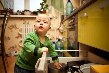 Fototapeta na wymiar Curious child opens kitchen drawer with dishes
