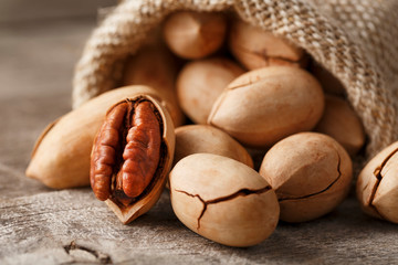 Pecans spill out of a bag on a wooden table, close-up. Peeled, in a shell.