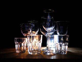 Close ups of wine-, long drink- and spirits-glasses on a wooden shelve in a bar, in front of a dark...