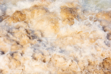 sea waves splash foam on the sunny beach.  mess of salt water and sand in evening light. dynamic nature texture